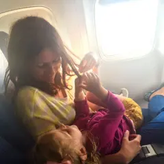 Mama bawi się włosami dziecka, szukając pomysłów, czym zająć dziecko w samolocie.