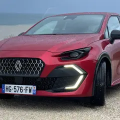 Nowe Clio 2026 w kolorze czerwonym, z nowoczesnym grillem i światłami LED, zaparkowane nad morzem.