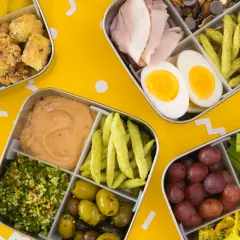 Four bento boxes filled with colorful, healthy foods, perfect for bento for beginners. Includes chicken, eggs, olives, grapes, and more.