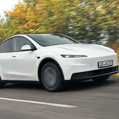 Biały Tesla Y w ruchu, otoczony rozmazanymi jesiennymi drzewami. Czy warto kupić?