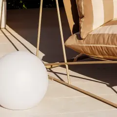 Una lámpara suelo esférica ilumina la terraza junto a un sillón a rayas.