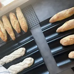 Gotowe do pieczenia bagietki po francusku, świeżo wyrośnięte ciasto i wypieczone bochenki na ruszcie.