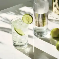 Orzeźwiający drink z limonką i lodem obok butelki wódki. Czy wódka ma gluten? Ta czysta wódka, destylowana z ziemniaków, jest bezglutenowa.