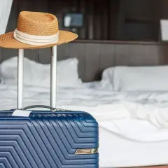 Błękitna walizka i słomkowy kapelusz gotowe do wyjazdu. Zastanawiasz się, co można zabrać z hotelu? Pamiętaj o swoich rzeczach!