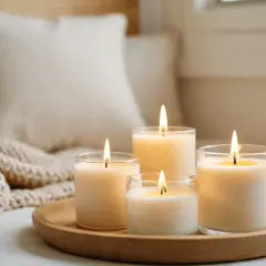 Velas encendidas en un plato de madera, rodeadas de mantas y cojines. Considera alternativas a la parafina, ya que la parafina es cancerígena.