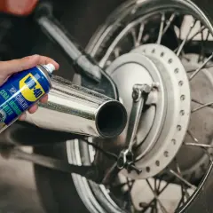 Mano che spruzza cera lucidante WD-40 su uno scarico cromato per lucidare la moto.