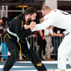 Dwóch zawodników BJJ w kimonach walczy na macie. Jeden w czarnym, drugi w białym.
