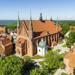 Zamek Frombork z lotu ptaka, z dominującą bazyliką katedralną i wieżami obronnymi, nad błękitną wodą Zalewu Wiślanego.