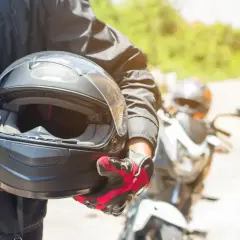 Motocyklista w czerwono-czarnych rękawicach trzyma kask. Warto wiedzieć, co to jest pinlock w kasku, by uniknąć parowania wizjera podczas jazdy.