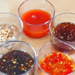 Five small glasses hold various Japanese dipping sauces, including a creamy peanut sauce, a bright red sauce, and a dark soy-based sauce with garlic.