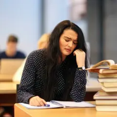Verzweifelte Studentin mit Büchern. Sie überlegt, ob sie das **uni wechseln** soll.