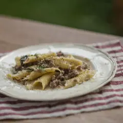 Pasta con ragú bianco, un plato reconfortante con carne picada y hierbas frescas, servido en un plato blanco sobre una servilleta a rayas.