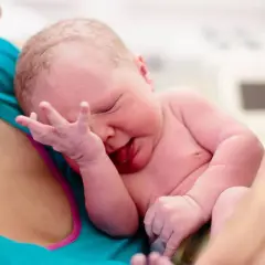 Neugeborenes Baby wird von der Mutter gehalten. Die Nabelschnur wird auspulsieren gelassen, um dem Kind alle wichtigen Nährstoffe zu übergeben.