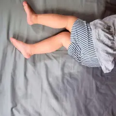 Gambe di bambino su lenzuola grigie. Un piccolo incidente notturno, forse legato all'enuresi notturna, ha lasciato un segno.