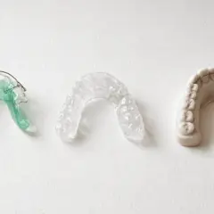 Tres dispositivos dentales: un retenedor verde, un retenedor transparente y un modelo de dientes con barra retenedora.