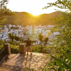 Hombre con brazos abiertos contempla un pueblo blanco en la sierra de Sevilla al atardecer.