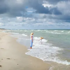Matka patrzy, jak dziecko bawi się w falach. Czy Szwecja ma dostęp do Morza Północnego? Tak, przez cieśniny Skagerrak i Kattegat.