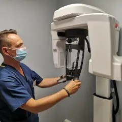 Medyk w maseczce przygotowuje pacjenta do badania CBCT na nowoczesnym sprzęcie stomatologicznym.
