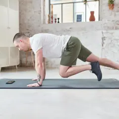 Un homme en short vert effectue un exercice de gainage latéral sur un tapis de yoga.