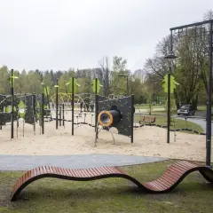 Nowoczesny plac zabaw w parku na zdrowiu z piaskownicą, ściankami wspinaczkowymi i nietypową ławką.