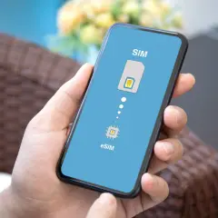 Dłoń trzyma smartfon z ekranem pokazującym ikonę karty SIM i chip eSIM, symbolizując przejście na technologię eSIM.