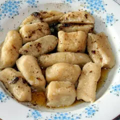 Gotowe pierogi leniwe, polane masłem i posypane cynamonem, czekają na talerzu z niebieskimi kwiatuszkami.