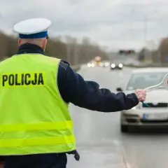 Policjant w kamizelce odblaskowej zatrzymuje samochód. Kierowca rozmawiający przez telefon może spodziewać się mandatu.