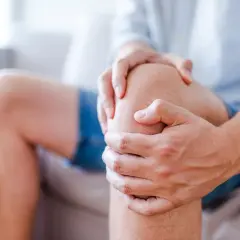 Mężczyzna trzyma się za kolano, odczuwając ból. Kłucie w kolanie utrudnia mu codzienne czynności.