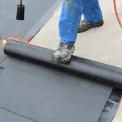 Arbeiter schweißt Bitumenbahn auf Garage Betondecke. Flammen erhitzen die Rolle für die Abdichtung.