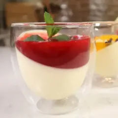 Panna cotta w szklankach z musem malinowym i miętą. Obok deser z musem mango.