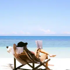 Relaks na plaży z książką – idealne miejsce na wakacje. Błękitne morze i biały piasek tworzą rajski krajobraz.