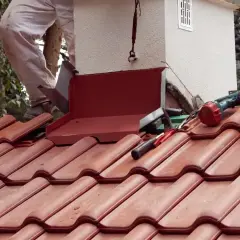 Prace dekarskie przy kominie, narzędzia i blacha. Może to być część prac związanych z tym, jak usunąć zapach sadzy z komina.