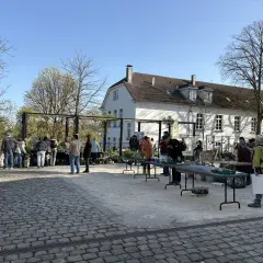 Menschen besuchen einen Markt mit Pflanzen und Ständen vor einem weißen Gebäude. Ein schönes Beispiel für Veranstaltungen in Bergisch Gladbach.