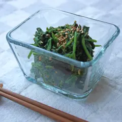 A glass bowl filled with spinach gomae, a savory sesame-dressed spinach dish, is ready to be enjoyed with chopsticks.