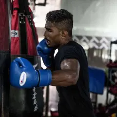 Boxer in blue gloves throwing a powerful cross punch at a heavy bag, sweat glistening on his arms.