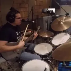Muzyk w słuchawkach gra na gitarze i perkusji, jakby wpadł w **rush tom sawyer**.