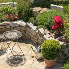 Terrasse mediterran gestalten: Ein kleiner Tisch mit zwei Stühlen lädt zum Verweilen ein, umgeben von Steinmauern und blühenden Pflanzen.