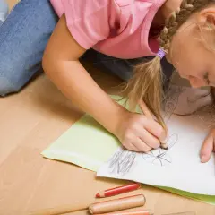 Dziewczynka w dżinsach i różowej bluzce rysuje kredkami, szukając zabawy na nudę.