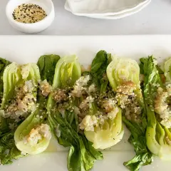 Bok choy tierno salteado con ajo y semillas de sésamo, servido en un plato blanco.