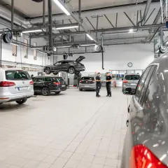 Bilverkstad med flera bilar, en lyft och mekaniker som diskuterar. Dags för volkswagen serviceintervall?