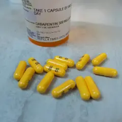 Żółte kapsułki leku Gabapentin 300 mg rozsypane obok butelki z lekiem.