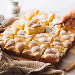 Ein frisch gebackener Ploatz, mit Puderzucker bestäubt, wird aus der Form gehoben. Ein köstliches Rezept für süße Momente.