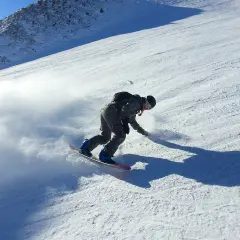 Snowboardzista w akcji na stoku, tworząc obłok śniegu. Idealne **deski do freeride** pozwalają na takie ewolucje.
