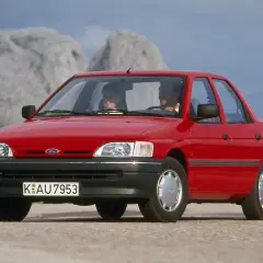 Czerwony Ford Orion z parą uśmiechniętych ludzi w środku, jadący po górskiej drodze.