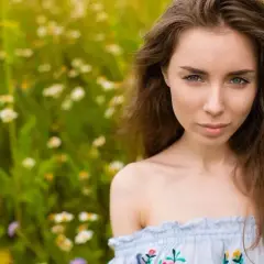 Kobieta z pięknymi, brązowymi włosami w stylu baleyage, w letniej sukience, na tle kwiecistej łąki.