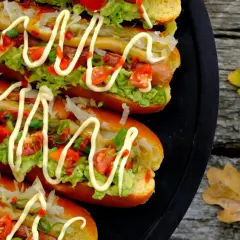 Fyra läckra completos chilenos med avokado, tomat och majonnäs på ett svart fat, redo att avnjutas utomhus bland höstlöven.