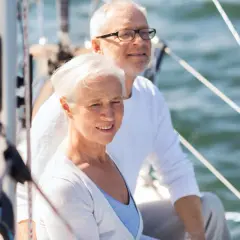Uśmiechnięta para seniorów na żaglówce. Idealne wczasy świąteczne dla samotnych seniorów, by poczuli się jak na romantycznym rejsie.