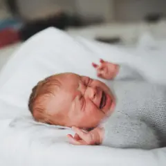 Malutkie 1,5 roczne dziecko rzuca się w nocy, ubrany w szary sweterek, leży na białej pościeli.