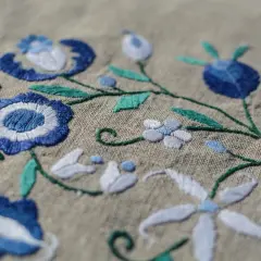 Un fichier broderie aux motifs floraux bleus et blancs sur fond beige. Les détails des points de couture sont visibles.
