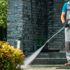 Mężczyzna w ogrodniczkach wykonuje impregnację kostki brukowej myjką ciśnieniową, chroniąc nawierzchnię przed zabrudzeniami i wilgocią.
